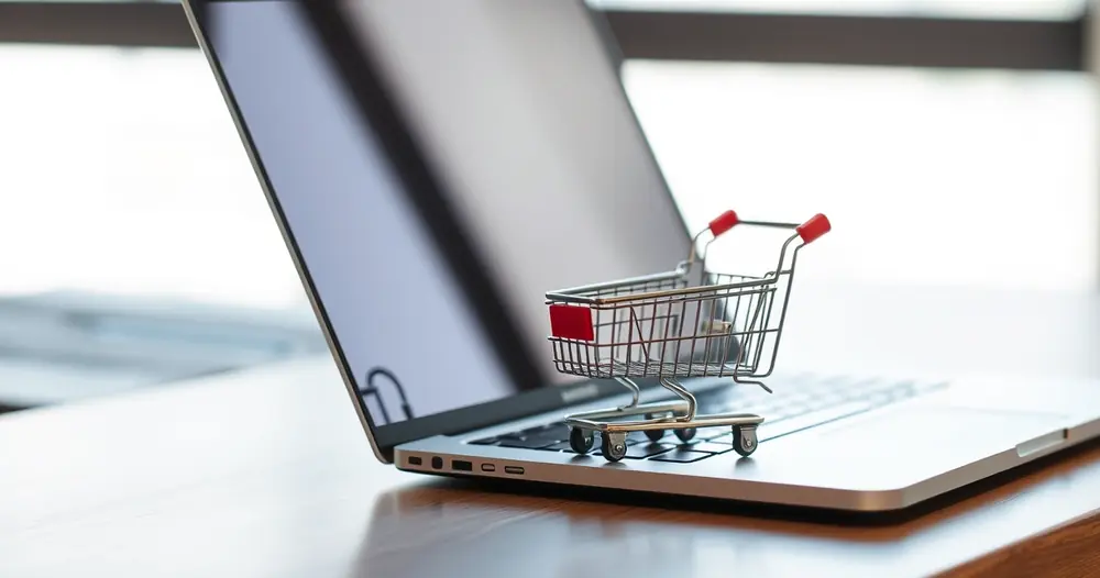 Carrinho de compras em miniatura ao lado de um notebook