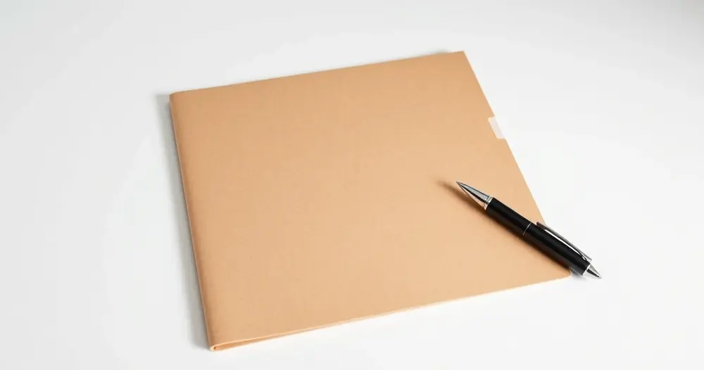 pasta de papel pardo fechada com caneta ao lado sobre mesa branca