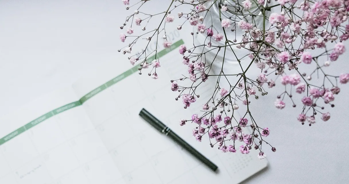 Agenda com calendário, caneta e flores sobre uma mesa, ilustrando a dor na barriga com ciclo irregular